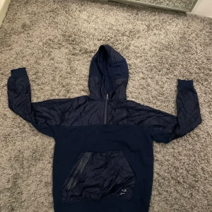 Mörkblå hoodie från Zara - Säljer en mörkblå hoodie från Zara med textdetaljer på huvan och ryggen. Hoodien har en dragkedja framtill och en stor ficka på magen. Perfekt för en avslappnad stil.
