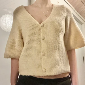 Beige stickad kofta - Så mysig beige stickad kofta med knappar framtill. Koftan har korta ärmar och v-ringning. Ser ingen storlek men uppskattar till S/M! 10% alpacka 💞