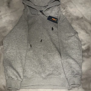 Grå hoodie från Polo Ralph Lauren - Säljer en stilren grå hoodie från Polo Ralph Lauren. Tröjan har en klassisk design med en liten broderad logotyp på bröstet och en praktisk dragkedja vid halsen. Perfekt för en avslappnad look. Storlek s sitter som xs 