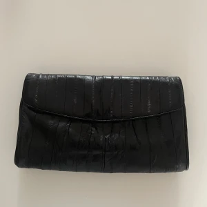 Vintage Black Leather Shoulder Clutch Bag - Vintage Black Leather Curved Bag with Detachable Shoulder Strap  Using panelled strips of Eel Leather, a luxurious material you don't see often that gives a beautiful texture & natural sheen to the bag. EU Only.  Magnetic Closure  1 Interior Zip Compartment + 1 Exterior Zip Compartment  Natural Vintage Wear, Very Good Condition  100% Leather  *16.5 CM/ 6.5 IN Length  *28 CM/ 11 IN Width  *36.5 CM/ 14.4 IN Drop  ***Please note, this item is only available to EU customers. 