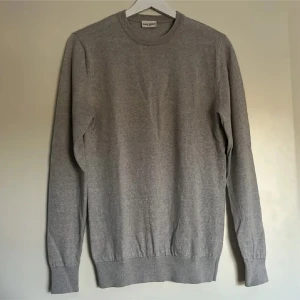 Grå merinoulltröja från John Henric - Säljer en stilren grå tröja från John Henric i 100% merinoull. Tröjan har en klassisk design med rund hals och långa ärmar, perfekt för kyligare dagar. Den är mjuk och bekväm, idealisk för både vardag och mer uppklädda tillfällen.