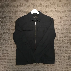 Mörkblå jacka från Lyle & Scott - Snygg svart jacka/overshirt från Lyle & Scott med dragkedja framtill. Jackan har en klassisk krage och två bröstfickor med lock. Perfekt för en stilren look.
