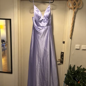 Syren lila balklänningar i satin - Elegant syrenlila balklänning i satin med djup v-ringning och smala axelband. Perfekt för balen! Den är aldrig använd!