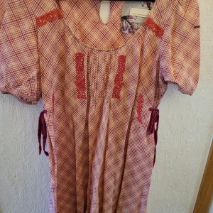 Rutig tunika med broderier från Odd Molly, stl 3 - Charmig rutig tunika från Odd Molly i rosa och vitt. Tunikan har korta ärmar och fina spetsdetaljer.. Den har även knytband i midjan för en justerbar passform. Perfekt för en avslappnad och stilfull look.