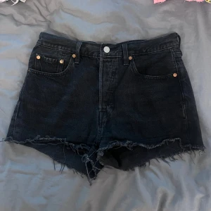 Svarta jeansshorts från Levi's - Snygga svarta jeansshorts från Levi's med fransig kant och klassisk femficksdesign. Perfekta för en avslappnad stil. De har en knappgylf och är tillverkade i slitstarkt denim.