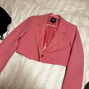 Rosa croppad kavaj från Zara - Säljer en snygg rosa croppad kavaj från Zara. Kavajen har en enkel knapp framtill och är perfekt för att ge en stilren look. Den har långa ärmar och en klassisk krage, kavajen är endast använd fåtal gånger men har fått lite fläckar på insidan där slagen är vikta men kommer säkert gå bort i tvätt då jag inte tvättat den. Säljs för 140kr