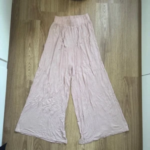 Ljusrosa vida byxor - Säljer ett par bekväma och luftiga ljusrosa byxor med hög midja. Byxorna har en loose passform och är tillverkade i ett mjukt material. Endast använda en gång.