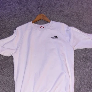 Vit tröja från The North Face - Säljer en vit tröja från The North Face med deras logga tryckt på bröstet och en stor logga på ryggen med texten 'Never Stop Exploring'. Köpt för 500kr 