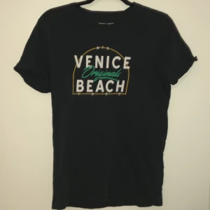 Svart t-shirt från Jack & Jones - Snygg svart t-shirt från Jack & Jones med tryck 'Venice Originals Beach' i vitt och grönt. Perfekt för en avslappnad stil. Regular fit och kortärmad design.
