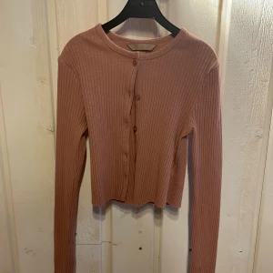 Rosa ribbad kofta från H&M - Säljer en söt rosa ribbad kofta från H&M. Den har långa ärmar och knappar framtill. Perfekt för lager-på-lager och att hålla sig varm under kyligare dagar. Passar bra till både jeans och kjol. Har använt den kanske 1 gång för flera år sedan. Storlek xs. Betalar inte frakt.