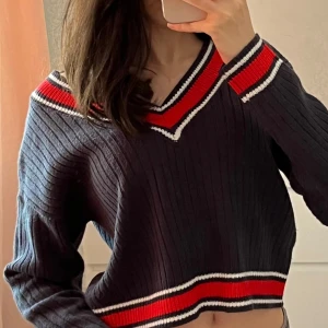 Marinblå stickad tröja - Stickad marinblå ribbad tröja med v-ringad hals och röd-vita ränder. Använd fåtal gånger, jätte bra skick i strl XS