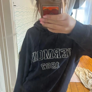 Mörkblå hoodie från Firefly - Säljer en mörkblå hoodie från Firefly med texten 'VERMONT 1987' tryckt på framsidan. Tröjan har en klassisk design med huva och dragsko. Perfekt för en avslappnad stil. Säljes för att jag inte har någon använding av den och bara använt den en gång tidigare😊
