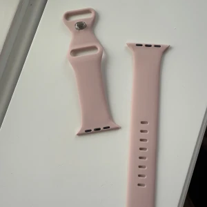 Rosa klockarmband Apple Watch  - Säljer ett stilrent rosa klockarmband i mjukt material. Perfekt för att ge din klocka en ny look. Armbandet har justerbara hål för att passa olika storlekar och en smidig stängning med metallknapp. Passar till Apple Watch 42/44/45 mm. Aldrig använt! 