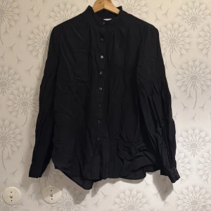 Svart skjorta från KappAhl - Snygg svart skjorta från KappAhl i storlek M. Skjortan har långa ärmar och knappar framtill. Perfekt för en stilren look.