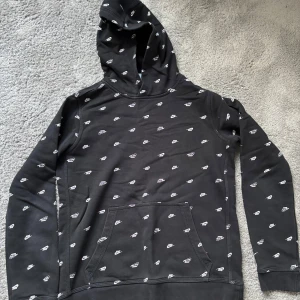 Svart Nike hoodie med mönster - Säljer en svart hoodie från Nike med all over print. Tröjan har känguruficka.