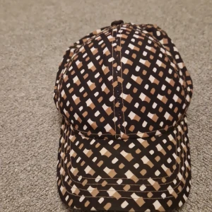 Mönstrad keps från Boss - Snygg keps från Boss med ett unikt mönster i svart, beige och brunt. Perfekt för att ge din outfit en cool touch. Justerbar passform för optimal komfort.