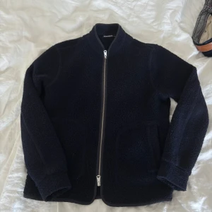 Marinblå  fleecejacka från J.Lindeberg - Säljer en marinblå fleecejacka från J.Lindeberg med dragkedja framtill. Jackan har en stilren design med långärmade ärmar och en mjuk, värmande känsla. Perfekt för våren