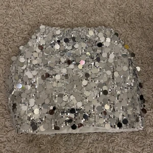 Glittrig silver kjol - Säljer en glittrig silver kjol täckt med stora paljetter. Kjolen är kort och perfekt för att dra blickarna till sig. Den har en tight passform som framhäver figuren. Perfekt för utekvällar eller festliga firanden. Fraktar endast varan och köparen betalar frakten! Priset som syns är vad som gäller🙏🫶