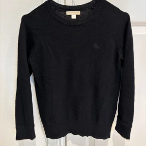 Svart tröja från Burberry - cashmere - Säljer en elegant svart kashmirtröja från Burberry. Tröjan har långa ärmar och en klassisk rund halsringning. Den är mjuk och perfekt för kyligare dagar. En subtil detalj är den vikta ärmslutet med ett diskret burberrymönster. 