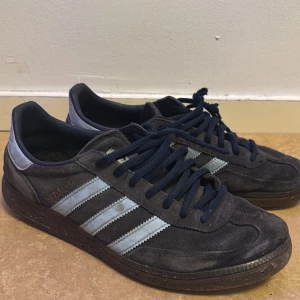 Adidas Samba i blå mocka - Säljer ett par klassiska Adidas Samba sneakers i grå mocka med ljusblå detaljer och snörning. Perfekta för en stilren och sportig look.