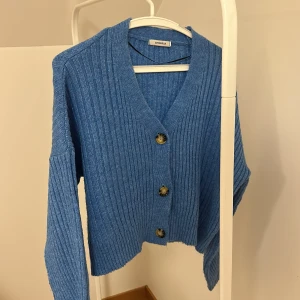 Blå ribbad kofta från Chiquelle - Säljer en snygg blå kofta från Chiquelle med ribbad design och stora knappar framtill. Perfekt för att hålla sig varm och stilren under kyligare dagar. Koftan har en v-ringad hals och långa ärmar.