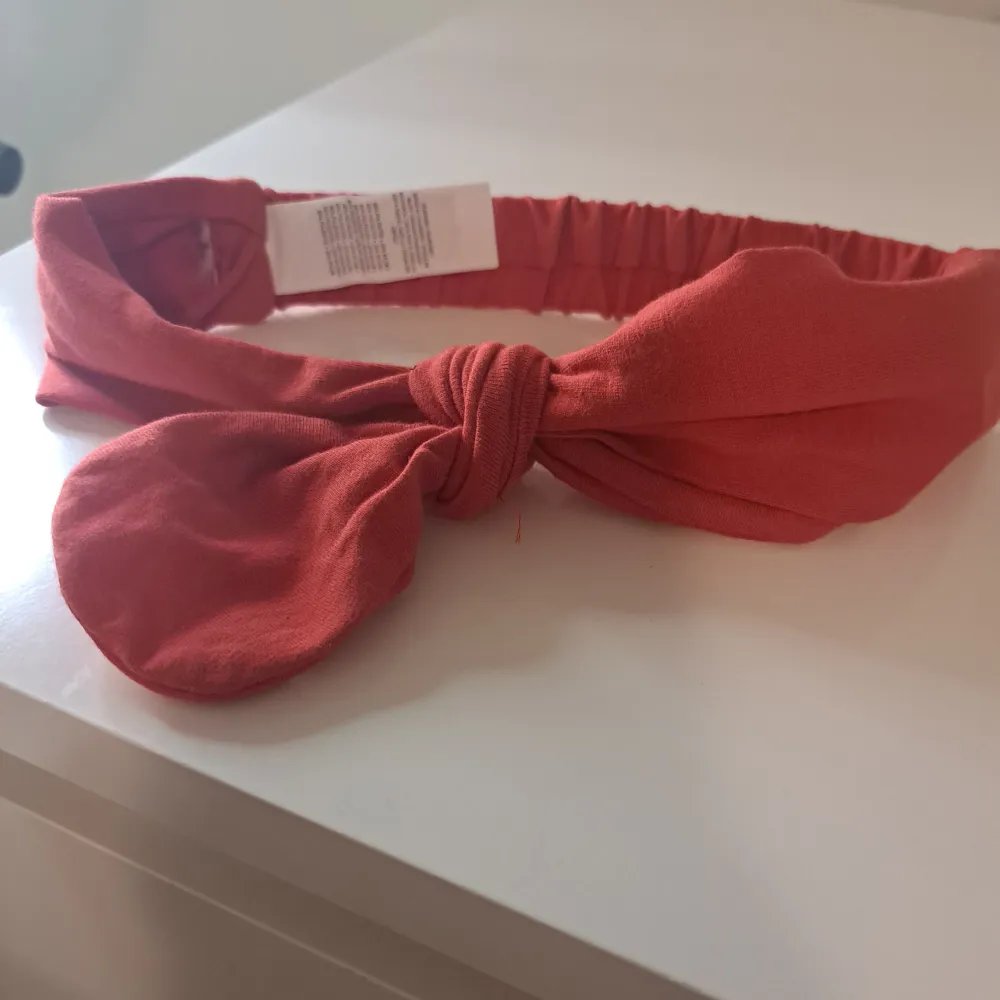 Snyggt rött diadem med en stor rosett framtill. Perfekt för att ge en färgklick till din outfit. Diademet har en elastisk del för bättre passform.. Asusteet.