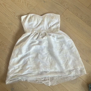Vit axelbandslös klänning (storlek s) - Säljer en vit axelbandslös klänning från Dark Pink som tyvärr är för stor. Klänningen har en glittrig yta och en dragkedja i ryggen. Storlek s. Perfekt till fest eller student ✨✨