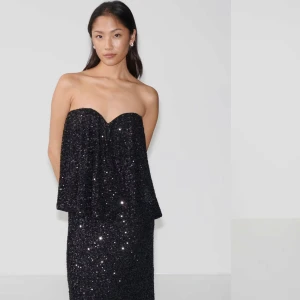 Svart glittrig axelbandslös topp - Snygg svart axelbandslös topp med glittrande paljetter. Perfekt för en kväll ute med en elegant touch. Toppen har en lös passform och en vacker glans som fångar ljuset. Köpt för 400