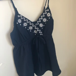 Svart broderad linnetopp - Snygg svart linnetopp med vita broderade blommor och justerbara axelband. Perfekt för varma dagar med en luftig passform och v-ringad design.                                                                                 Perfekt till sommaren ❤️