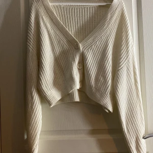 Vit ribbad kofta - Säljer en stilren vit ribbad kofta med knappar framtill. Koftan har en croppad passform och långa ärmar, perfekt för lager på lager-stil. Den är både mysig och trendig, idealisk för kyligare dagar.