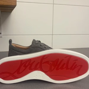 Grå sneakers från Christian Louboutin - Snygga grå sneakers från Christian Louboutin med den ikoniska röda sulan. Skorna har en stilren design med snörning och är tillverkade i mocka. Perfekta för dig som vill ha en touch av lyx i vardagen. Skorna är i storlek 42 men rymmer en 43.