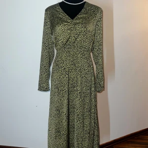 Grön leopardmönstrad klänning - Snygg grön klänning med leopardmönster och v-ringning. Klänningen har långa ärmar och en elastisk midja för en bekväm passform. Perfekt för att sticka ut med stil!