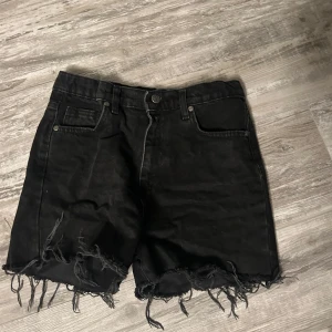 Svarta jeansshorts med fransar - Coola svarta jeansshorts med fransiga kanter. Perfekta för en avslappnad stil med en edgy touch. De har en klassisk ficksdesign och knappgylf.