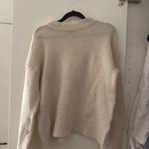 Beige stickad tröja - Mysig beige stickad tröja med långa ärmar och ribbad krage. Perfekt för kyliga dagar och ger en avslappnad look. Passar bra till jeans eller kjol för en stilren outfit.