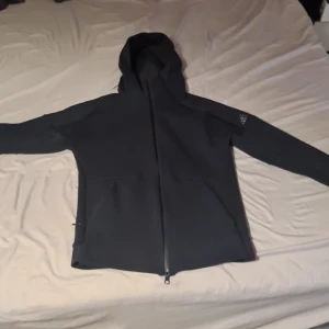 Svart hoodie med dragkedja - Säljer en svart hoodie med dragkedja och huva. Perfekt för en avslappnad stil. Den har långa ärmar och två fickor framtill. Enkelt och stilrent plagg för vardagsbruk.