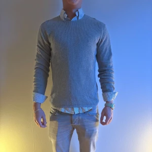 Mango Grå stickad tröja - Säljer en stilren grå stickad tröja med rund hals. Perfekt för lager-på-lager-look med skjorta under. Tröjan har långa ärmar och en klassisk passform. Passar både till jeans och chinos för en avslappnad stil.