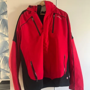 Röd och svart jacka från Craft - Säljer en snygg röd och svart jacka från Craft. Jackan har flera praktiska dragkedjor och en justerbar huva. Perfekt för utomhusaktiviteter med sin sportiga design och funktionella detaljer.