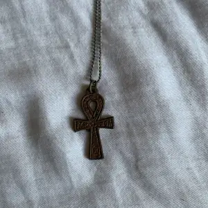 Snyggt halsband med ett ankh-hänge i brons. Kedjan är tunn och smidig, vilket gör den lätt att bära. Ankh-symbolen är detaljerad och ger en cool, mystisk känsla. Perfekt för dig som gillar unika smycken med en touch av goth stil.