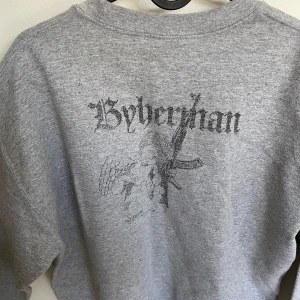 Grå sweatshirt från byherman - Säljer en grå sweatshirt med ett unikt tryck på framsidan. Tröjan är tillverkad i en mjuk bomullsblandning och har en avslappnad passform. Perfekt för en casual look.