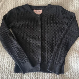 Svart kofta från C'est la vie - Säljer en svart kofta från C'est la vie. Den är stickad med ett fint kabelmönster och har långa ärmar. Koftan har knappar hela vägen fram. Koftan har inga defekter. Kontakta mig om du har fler frågor 😊