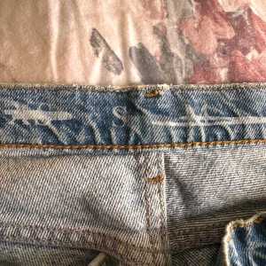 Slitna jeans från Never Denim - Säljer ett par coola, slitna jeans från Never Denim. De är ljusblå med snygga slitningar vid knäna och en skön, avslappnad passform. Perfekta för en casual look!