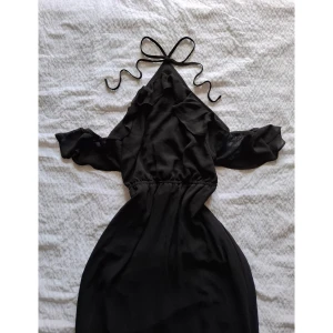 Svart halter-maxiklänning - Maxiklänning med detaljer i mesh. Off-shoulder volanger med resår samt volanger på klänningens botten.  Rygglös och knyts bakom nacken. Superfin och helt oanvänd (orginalprislapp fortf. kvar)  Säljer pga fel storlek