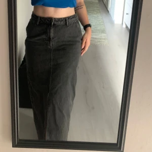 Svart långkjol i jeansmaterial - Säljer en snygg svart långkjol i jeansmaterial. Kjolen har en klassisk design med knapp och dragkedja framtill. enbart använd ett fåtal gånger 🖤