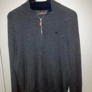 Grå tröja med dragkedja från Morris - Säljer en stilren mörkgrå tröja från Morris. Tröjan har en normal passform. Krympt från L till M och passar dig runt 180 cm.