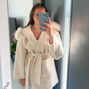 Fur Stockholm kappa - Kappa från märket Fur Stockholm. Storlek S. Färg: off white. Kappan är gjord av en ull mix med justerbart band i midjan. Luva med äkta päls som även är avtagbar. Kappan är använd endast ett fåtal gånger och är helt fri från fläckar.🩷Nypris 2199 kr.