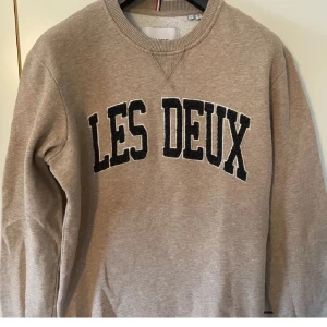 Beige sweatshirt från Les Deux - Säljer en snygg beige sweatshirt från Les Deux. Den har en klassisk rund halsringning och stora mörkgröna bokstäver på framsidan. Perfekt för en avslappnad stil och passar till både jeans och joggers. Superbekväm och stilren! Nypris 1200