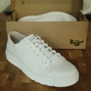 Vita snörskor i Venice-läder från Dr. Martens - Helt nya Dr. Martens-sneakers av modellen Dante i vitt läder. Avskalad och stilren design som gör att de passar till i princip vilka kläder som helst.  Jag brukar i regel köpa wide-modeller av skor då jag har breda fötter. Dessa har normal passform. Jag tog en vända runt kvarteret och konstaterade sedan att de var för smala för mina fötter.   Obs: De har legat på vinden ett tag och när jag letade hittade jag inte rätt låda. Jag hittade dock en annan Dr. Martens-låda som jag skickar dem i.  Hänvisar till Dr. Martens hemsida för ytterligare detaljer: https://www.drmartens.com/se/se/dante-sn%C3%B6rskor-i-vit-venice-l%C3%A4der-vit/p/2212710