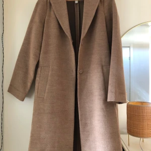 Beige kappa - Snygg beige kappa med klassisk design och knälång passform. Nyskick, slutsåld på hemsidan! Storlek 34 (XS). 