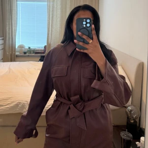 Brun skinnjacka med bälte - Snygg brun skinnjacka med bälte i midjan och långa ärmar. Jackan har en klassisk krage och knappar framtill. Perfekt för en stilren look. H&M