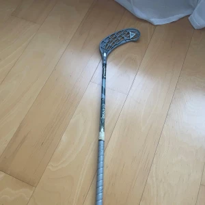 Grå innebandyklubba från Unihoc - Säljer en grå innebandyklubba från Unihoc med ett snyggt mönster och lindat grepp. Perfekt för både träning och match. Klubban har en böjd bladform för bättre bollkontroll. Hör av dig vid intresse! 🏑